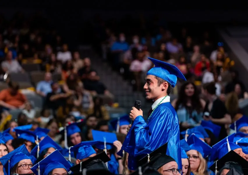 A high school graduate stands while speaking to his peers