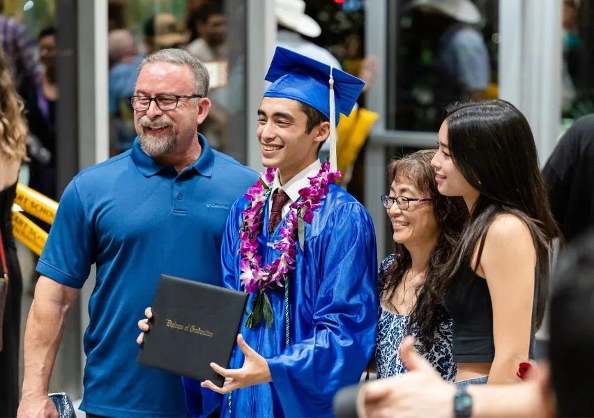Graduate proudly holds his diploma and takes a photo with his family