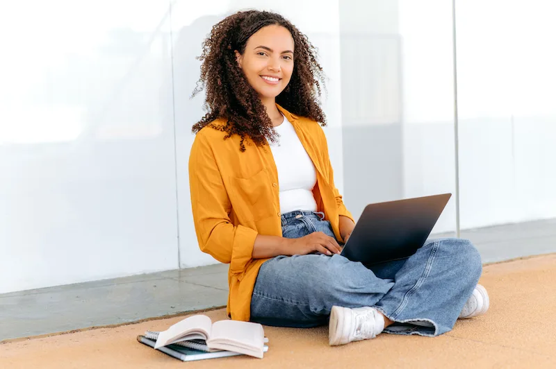 Female student with laptop. Education concept. Gorgeous stylish curly haired hispanic girl, sit near the university campus, using laptop, working on a project, looking at camera, smile friendly