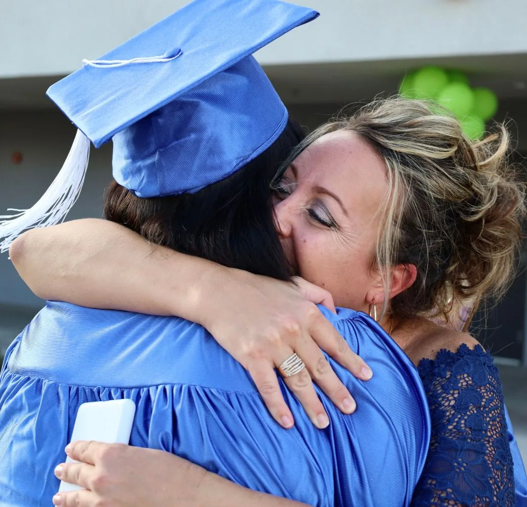 A HS Graduate receiving a hug at graduation from their mentor.